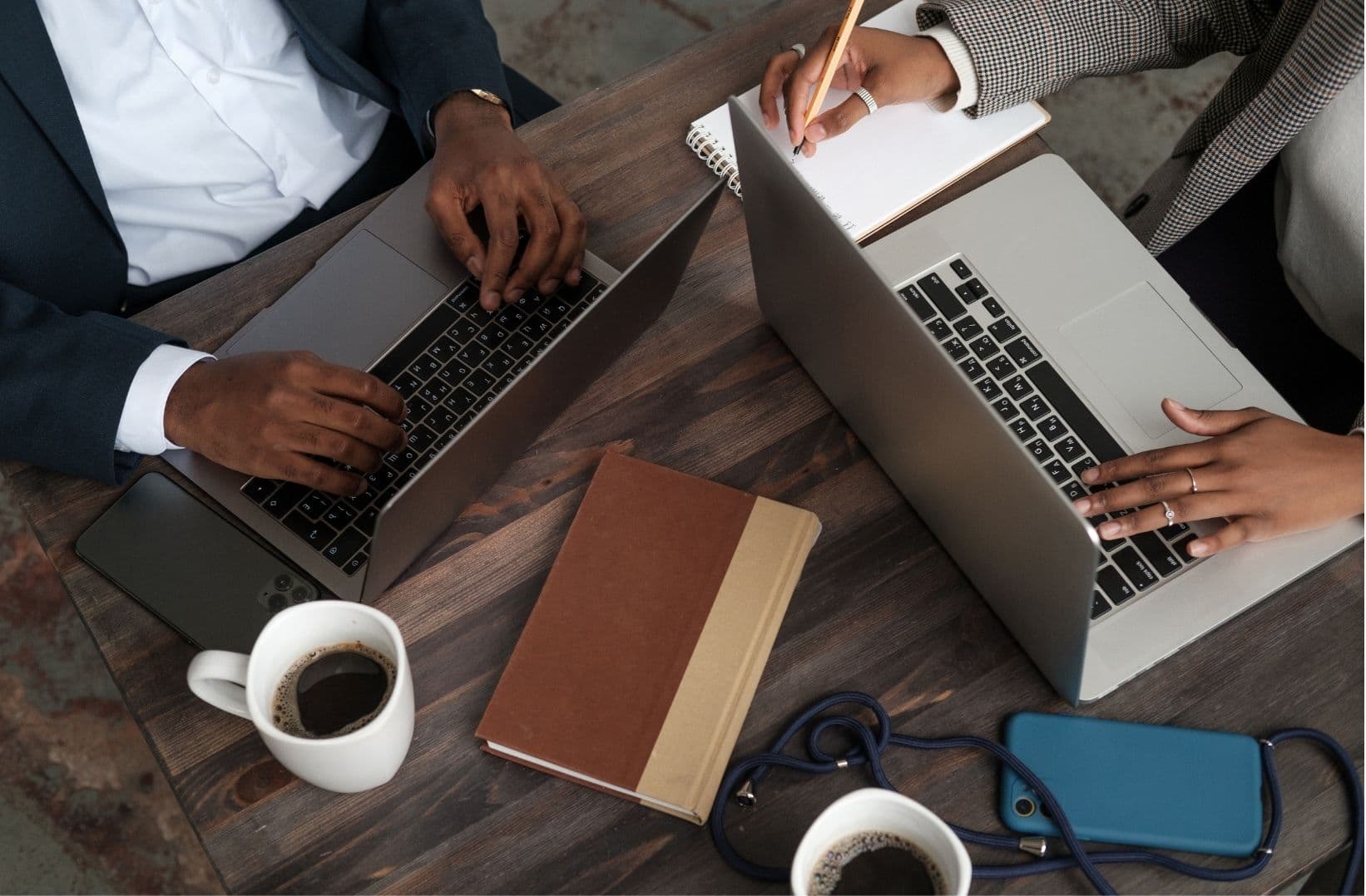 Two colleagues working side by side on laptops with coffee and a notebook
