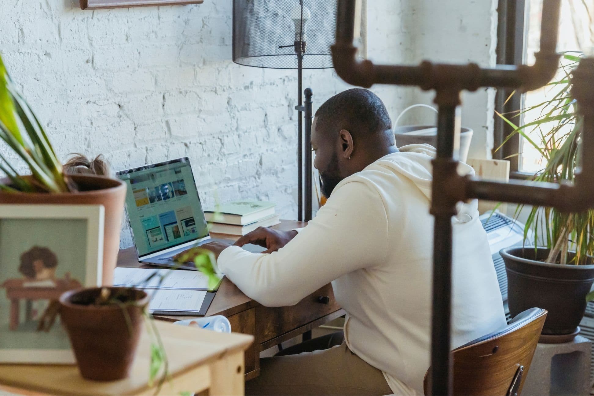 A person working on a laptop at a home desk with plants