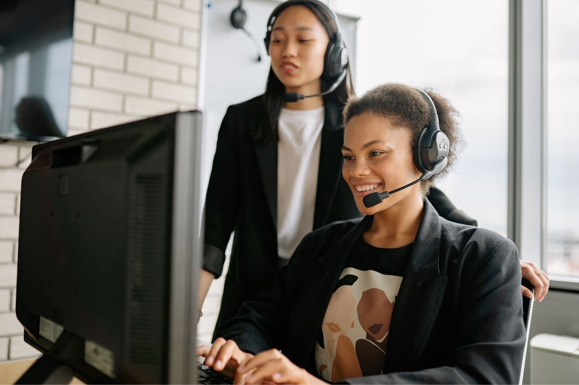 Two Aquifon support agents wearing headsets, helping a customer at a workstation
